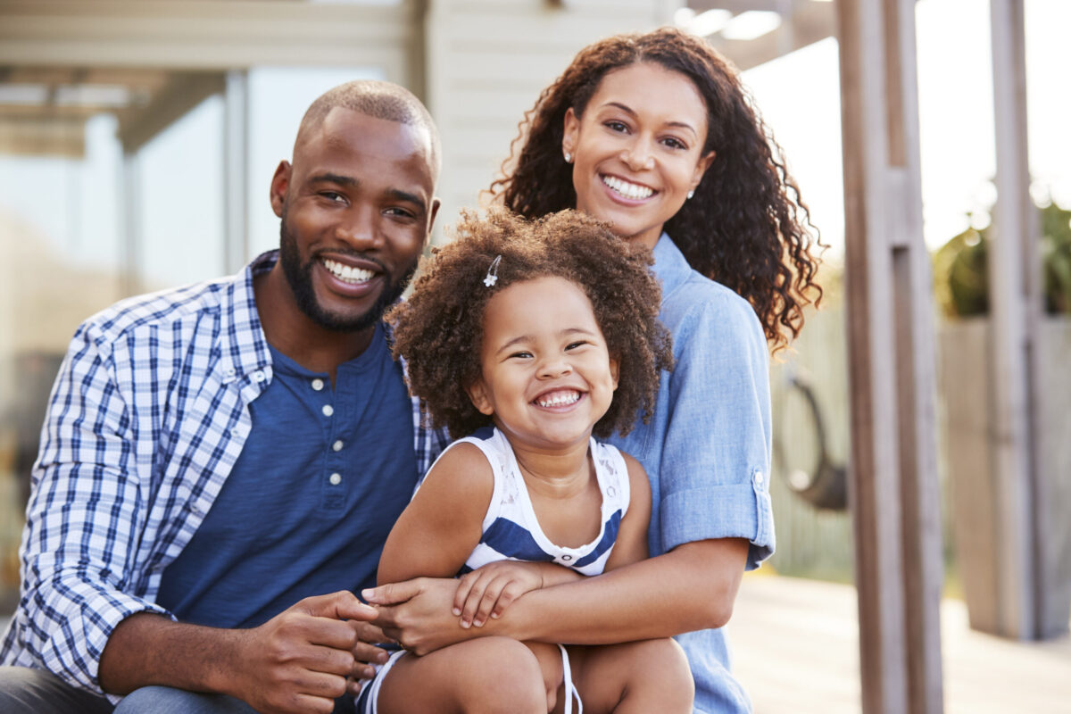 Young black family embracing outdoors and smiling at camera complimentary consultation